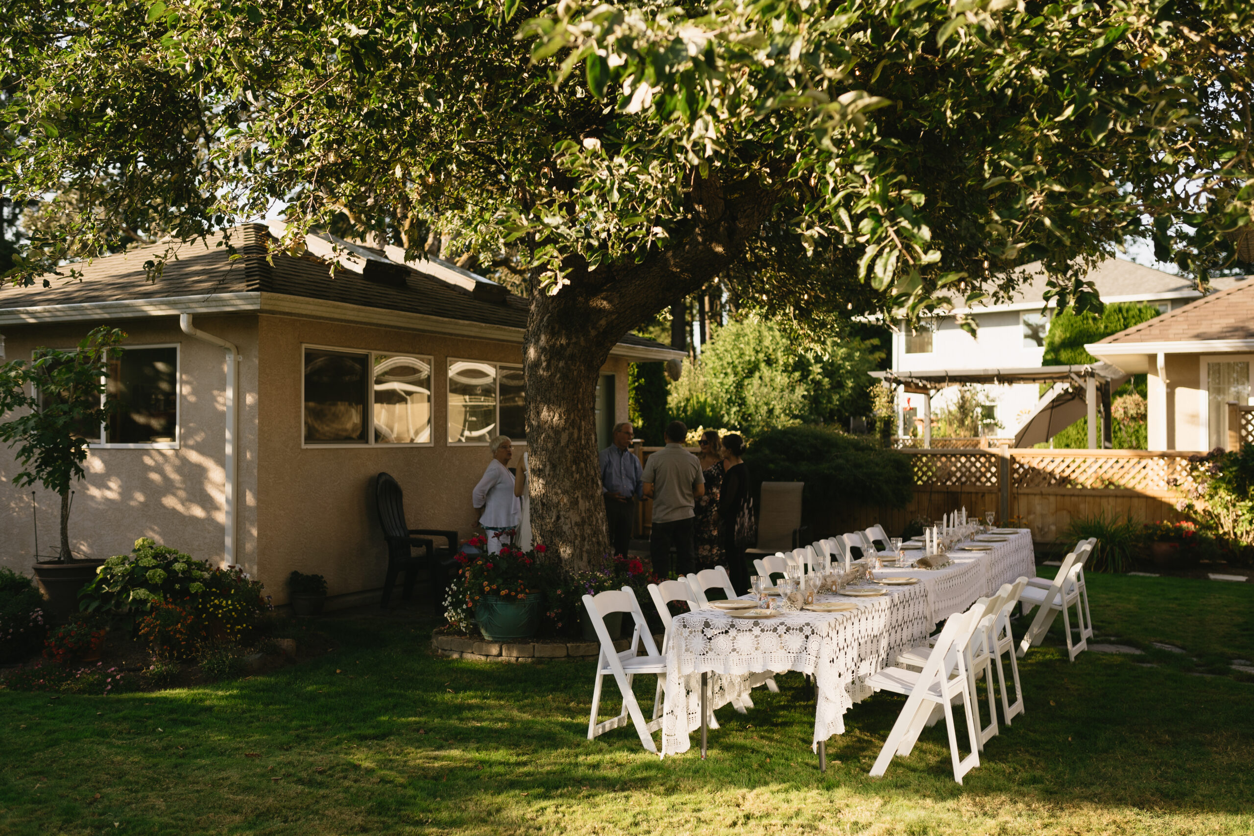 White dinner table under an apple tree at backyard wedding reception