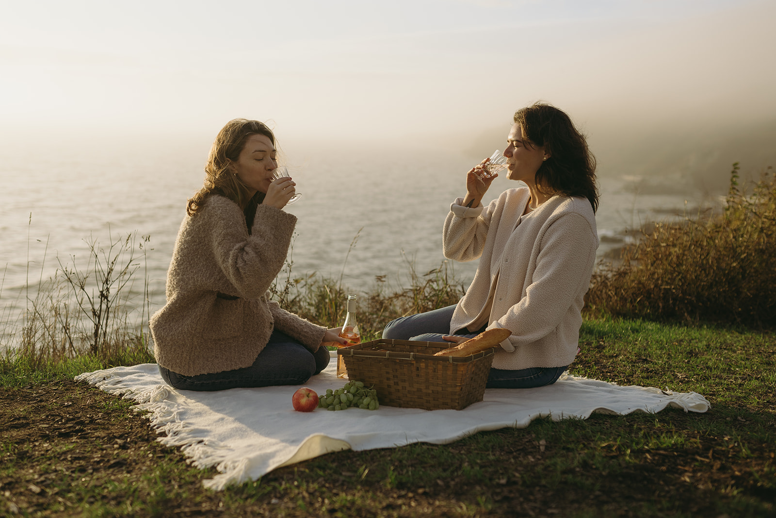 Two women enjoying a picnic by the ocean for their engagement photo shoot