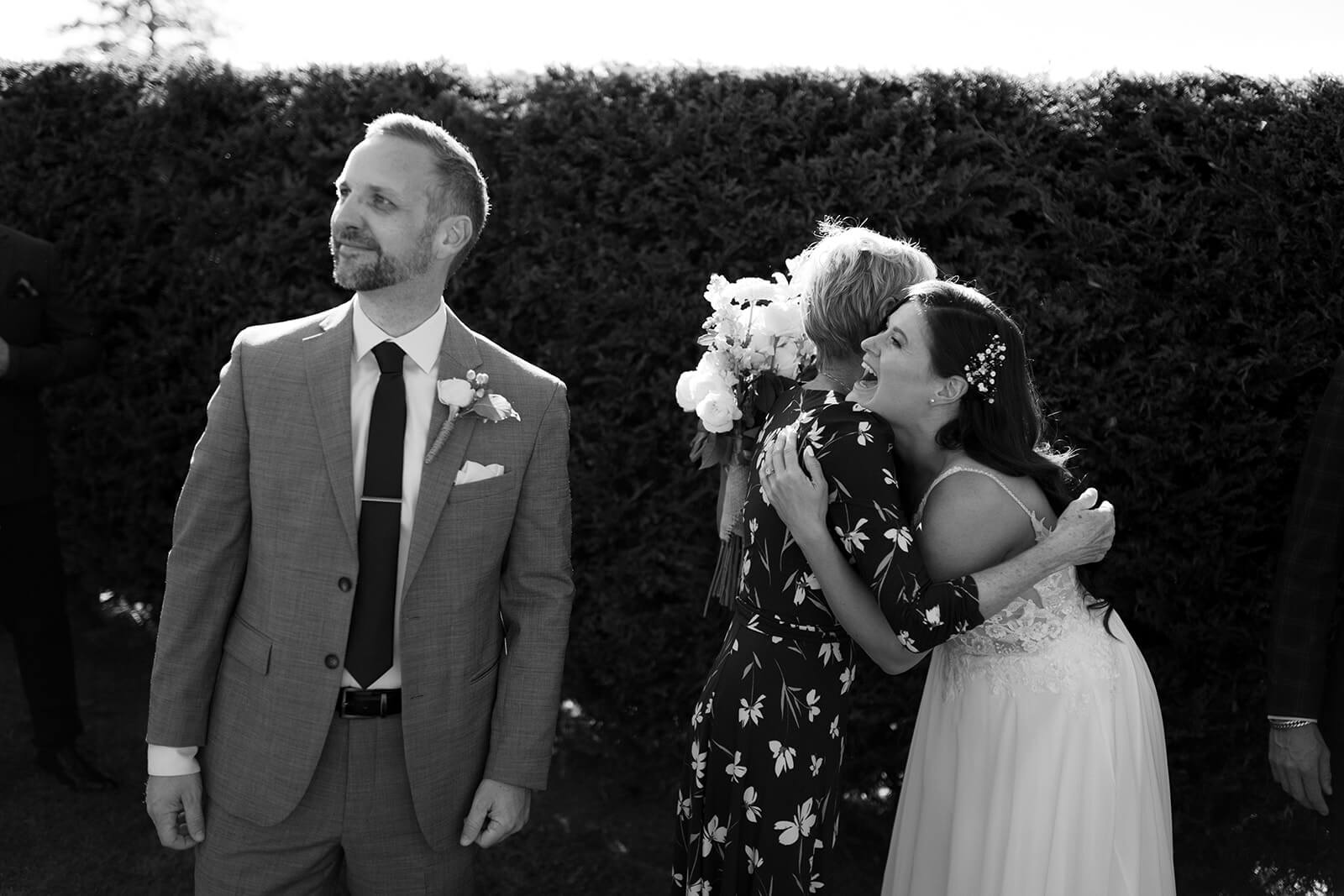 Bride hugging someone while groom looks off camera at Langtry Walk wedding